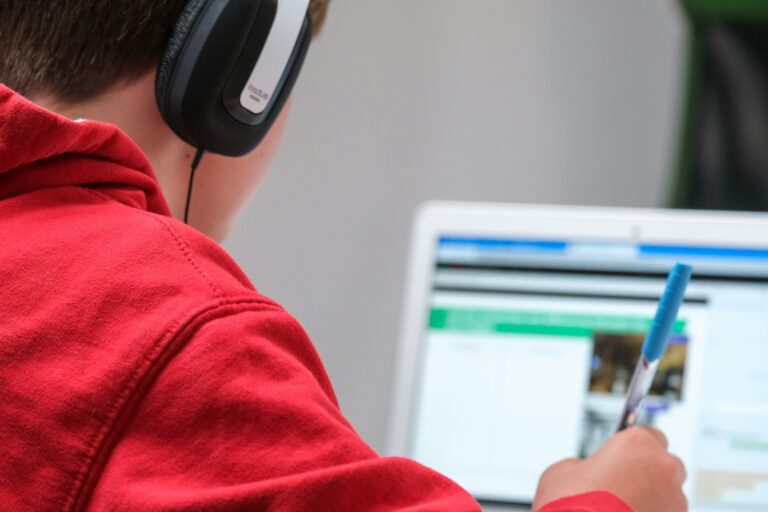 Junge mit Kopfhörern und Stift in der Hand lernt am Computer